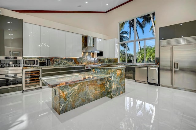 kitchen with dark stone countertops, beverage cooler, appliances with stainless steel finishes, wall chimney range hood, and modern cabinets