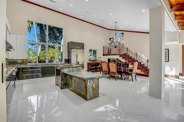 interior space with under cabinet range hood, built in refrigerator, a towering ceiling, a notable chandelier, and modern cabinets