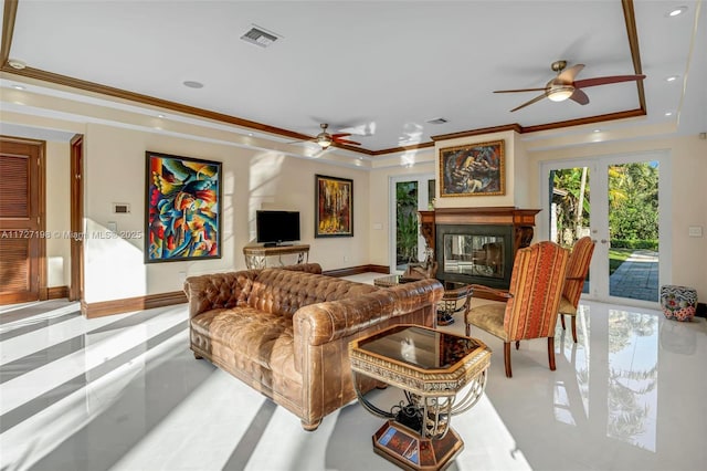 living area with visible vents, crown molding, baseboards, a tray ceiling, and a glass covered fireplace