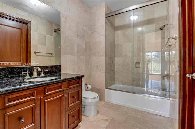 bathroom featuring toilet, tile walls, decorative backsplash, enclosed tub / shower combo, and vanity