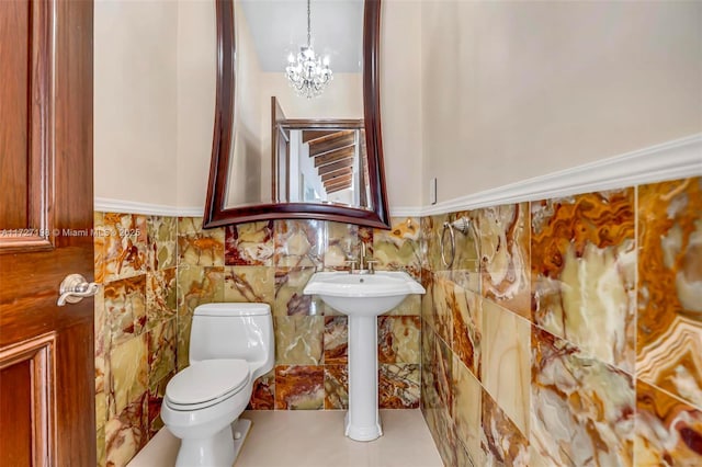 half bathroom featuring a notable chandelier, toilet, and tile walls