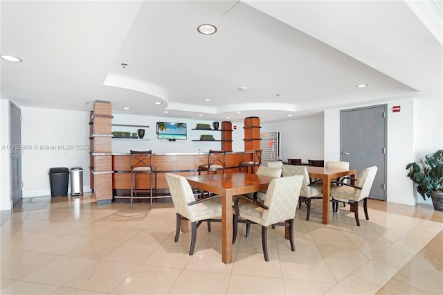 dining space with a raised ceiling, light tile patterned floors, and ornamental molding