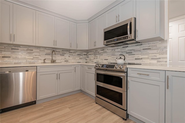 kitchen featuring tasteful backsplash, appliances with stainless steel finishes, sink, and light hardwood / wood-style flooring