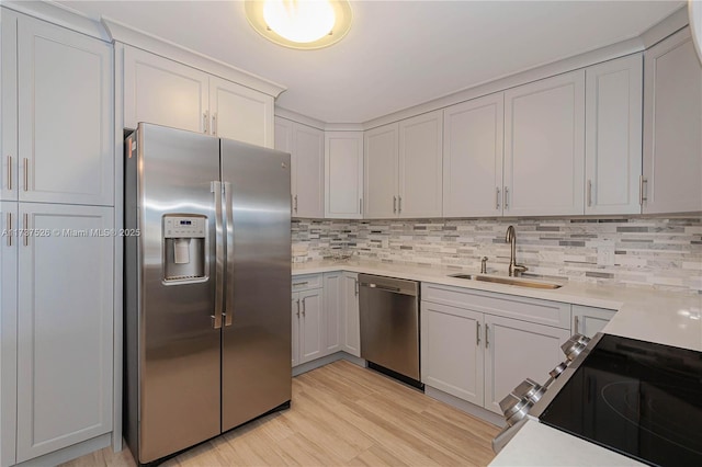 kitchen featuring sink, stainless steel appliances, tasteful backsplash, white cabinets, and light wood-type flooring