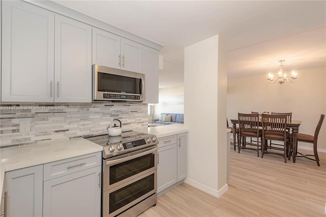 kitchen featuring tasteful backsplash, a chandelier, hanging light fixtures, light hardwood / wood-style flooring, and appliances with stainless steel finishes