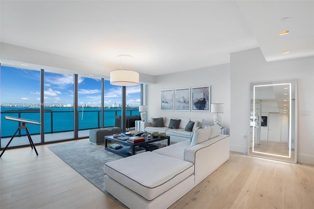 living room with floor to ceiling windows, a water view, and light wood-type flooring