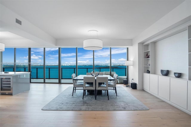 dining room with built in features, beverage cooler, expansive windows, light hardwood / wood-style floors, and a water view