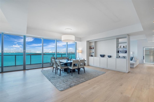 dining room with a water view, a wall of windows, light hardwood / wood-style flooring, and built in features