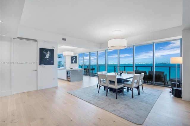 dining space with sink, a water view, light hardwood / wood-style floors, expansive windows, and beverage cooler