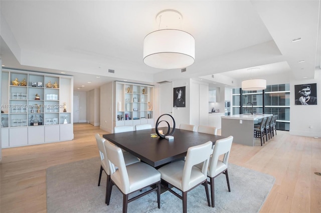 dining area featuring sink, a tray ceiling, and light hardwood / wood-style flooring