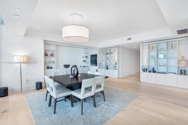 dining area with built in shelves, a raised ceiling, and light hardwood / wood-style flooring