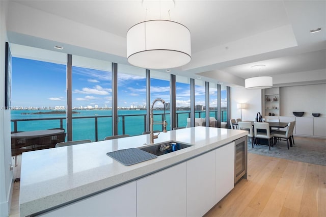 kitchen with sink, white cabinets, light stone counters, a water view, and light wood-type flooring