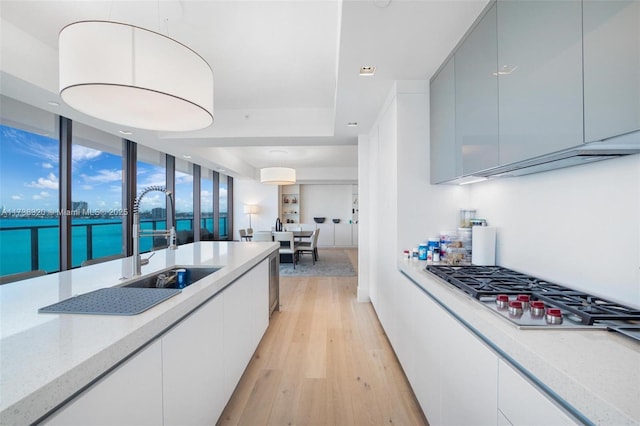 kitchen featuring sink, stainless steel gas cooktop, a water view, light stone counters, and light wood-type flooring