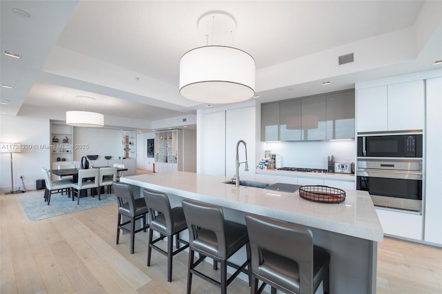 kitchen featuring pendant lighting, sink, a kitchen island with sink, stainless steel appliances, and white cabinets