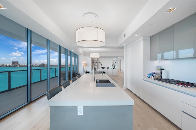 kitchen featuring stainless steel gas stovetop, white cabinets, hanging light fixtures, light hardwood / wood-style floors, and a center island with sink