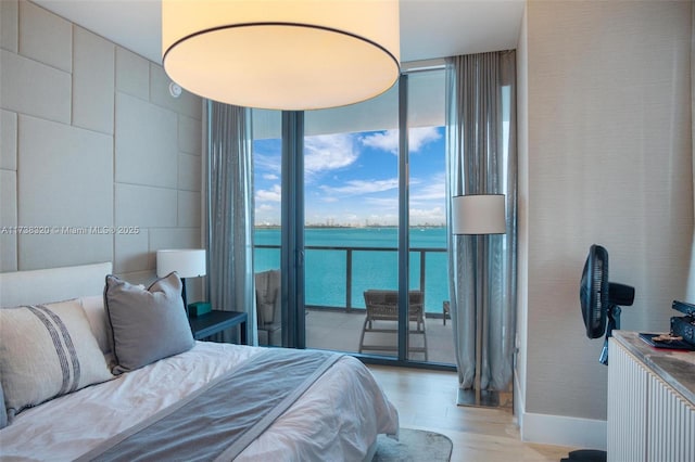 bedroom with light hardwood / wood-style flooring, access to outside, a wall of windows, and a water view