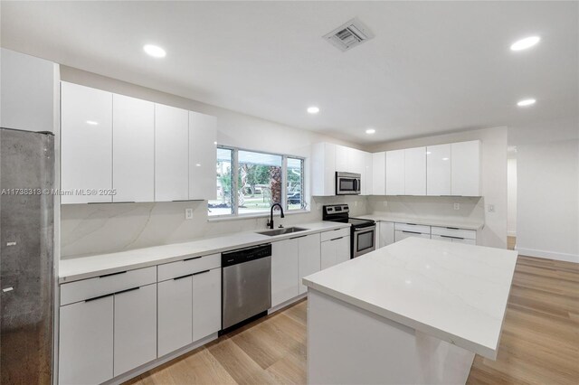 kitchen with a kitchen island, sink, white cabinets, stainless steel appliances, and light wood-type flooring