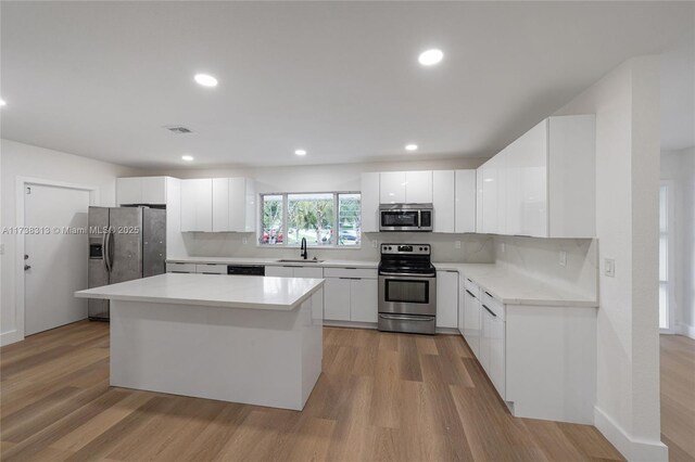 kitchen with a kitchen island, sink, white cabinets, stainless steel appliances, and light wood-type flooring