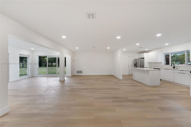 kitchen with a kitchen island, appliances with stainless steel finishes, white cabinetry, sink, and light hardwood / wood-style flooring