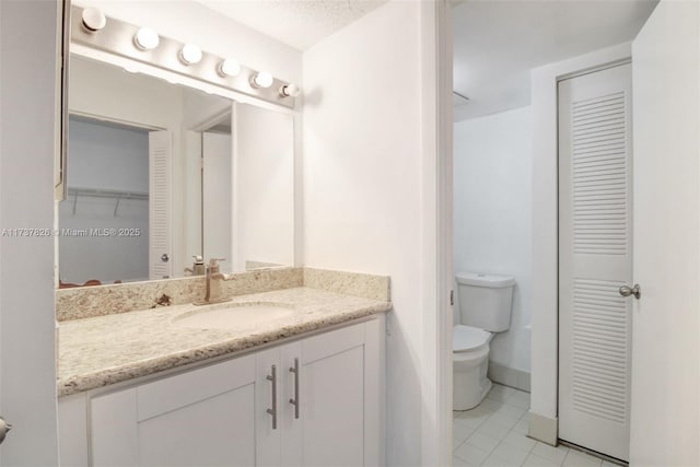 bathroom featuring baseboards, toilet, tile patterned flooring, vanity, and a closet