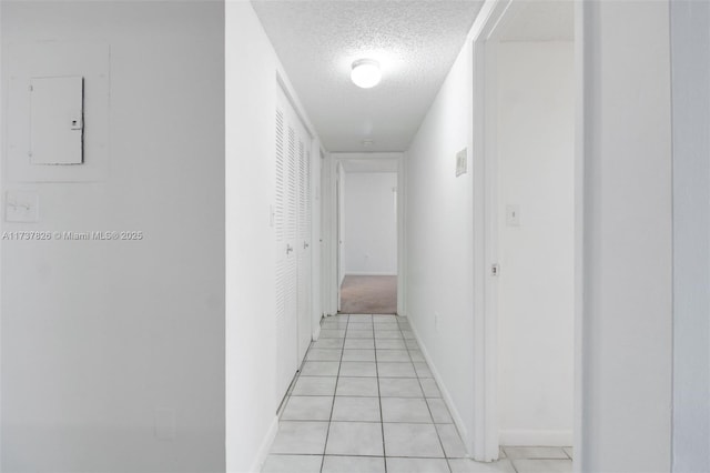 corridor featuring light tile patterned floors, baseboards, and a textured ceiling