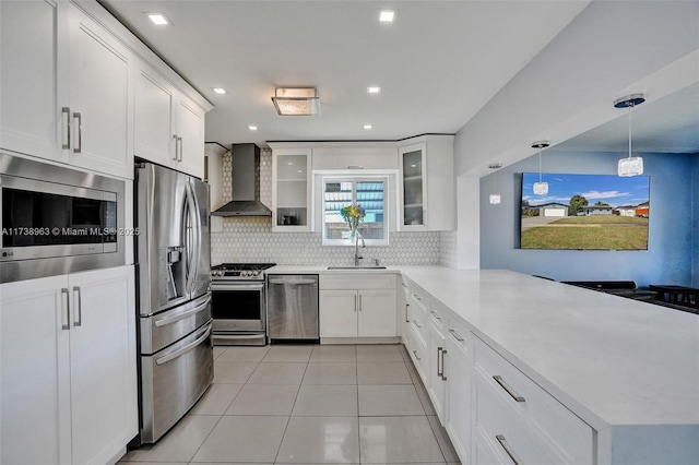 kitchen with sink, white cabinetry, decorative light fixtures, appliances with stainless steel finishes, and wall chimney range hood