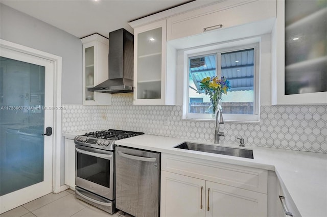 kitchen with light tile patterned flooring, white cabinetry, sink, stainless steel appliances, and wall chimney range hood