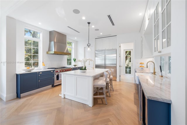 kitchen featuring a breakfast bar area, blue cabinetry, white cabinets, high quality appliances, and wall chimney exhaust hood