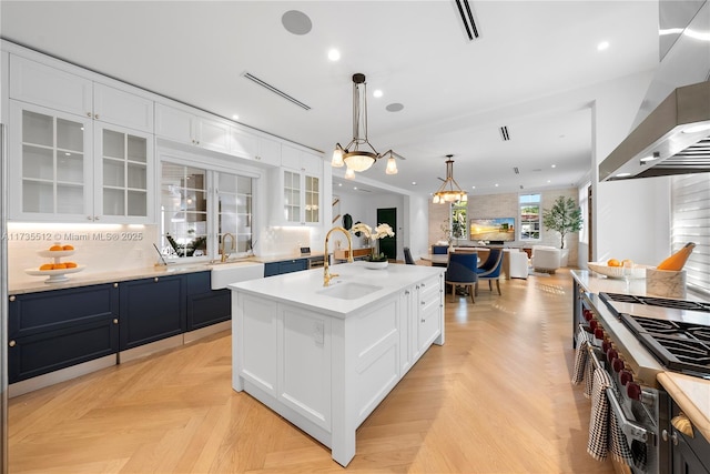 kitchen with extractor fan, sink, white cabinets, double oven range, and a kitchen island with sink