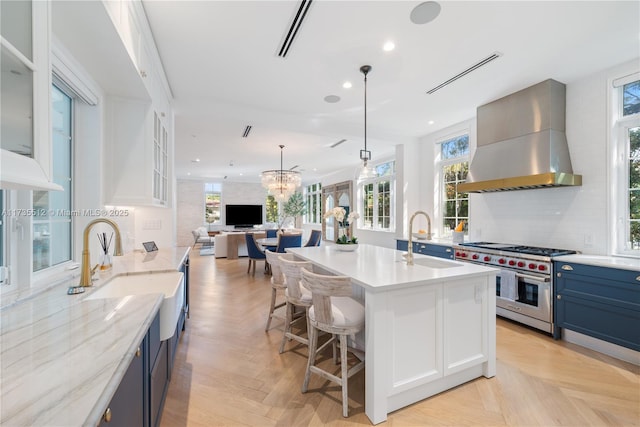 kitchen featuring visible vents, wall chimney exhaust hood, blue cabinets, luxury range, and a sink