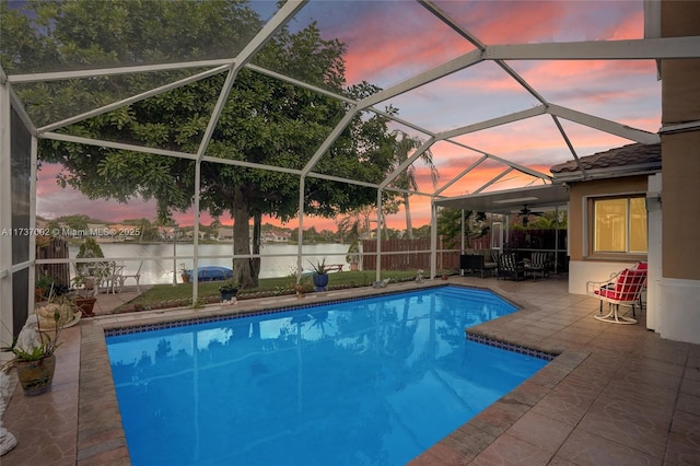 pool at dusk featuring a water view, ceiling fan, a lanai, and a patio area