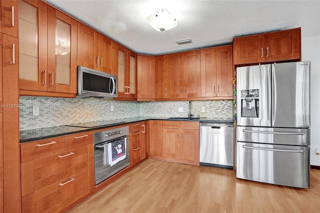 kitchen with sink, a textured ceiling, light wood-type flooring, appliances with stainless steel finishes, and decorative backsplash