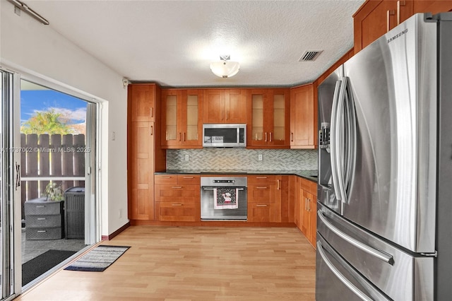 kitchen with stainless steel appliances, light hardwood / wood-style floors, a textured ceiling, and backsplash