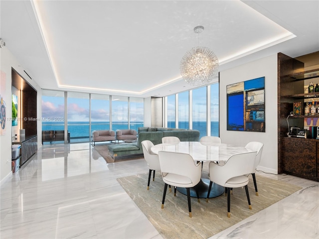 dining space with a tray ceiling, floor to ceiling windows, a chandelier, and a water view