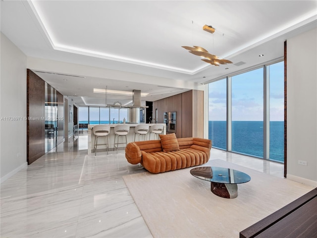 living room with a tray ceiling, a wall of windows, and a water view