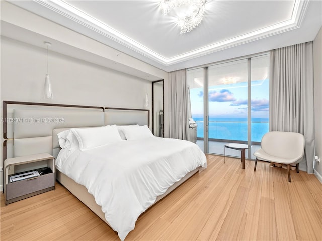 bedroom with a water view, crown molding, wood-type flooring, access to outside, and a tray ceiling