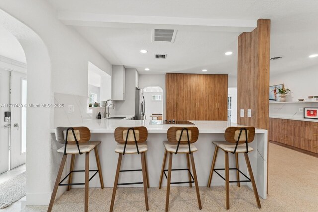 kitchen with a peninsula, brown cabinetry, light countertops, and freestanding refrigerator