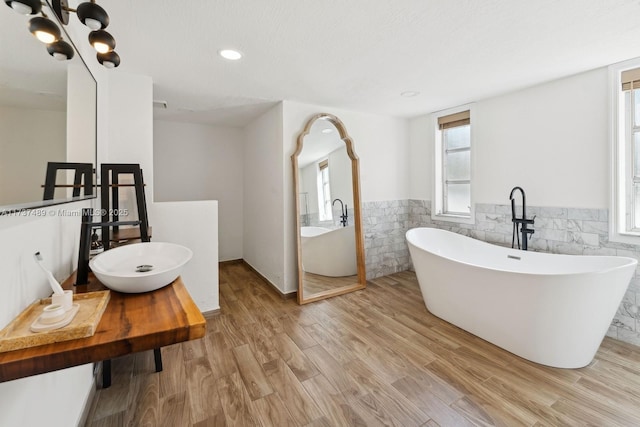 bathroom with a freestanding tub, a wainscoted wall, a sink, wood finished floors, and tile walls