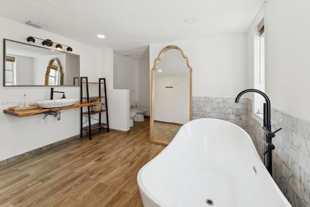 bathroom featuring wood finished floors, visible vents, tile walls, a freestanding bath, and a bidet