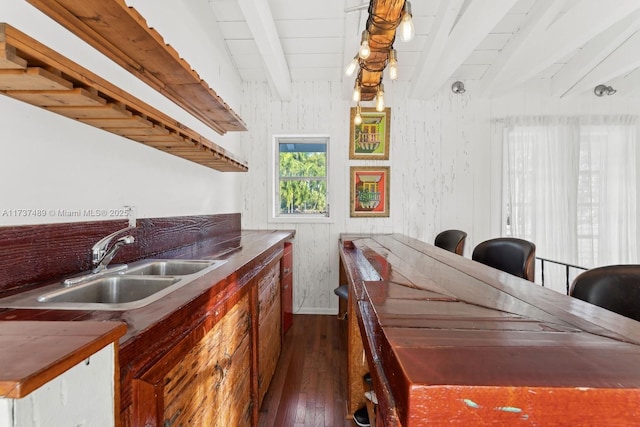 kitchen featuring dark wood-style floors, beamed ceiling, a sink, and wooden walls