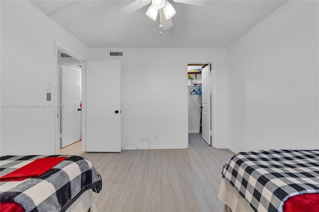 bedroom featuring ceiling fan, visible vents, baseboards, light wood finished floors, and a spacious closet