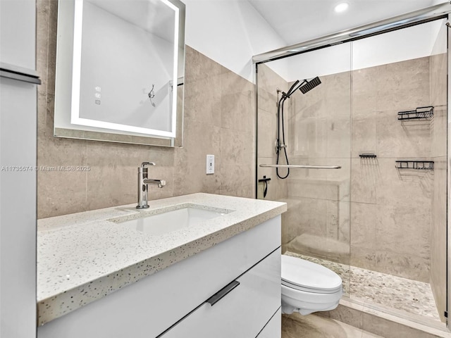 bathroom featuring vanity, a shower with shower door, tile walls, and toilet