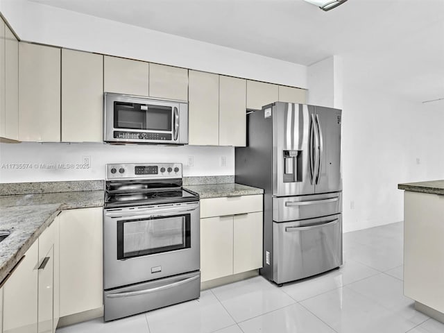 kitchen with cream cabinets, light tile patterned flooring, stainless steel appliances, and stone countertops