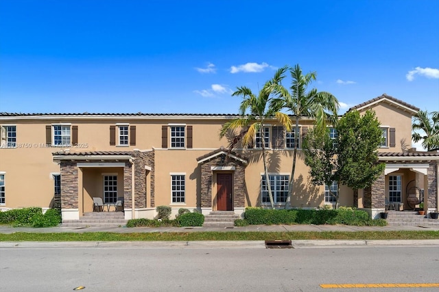 multi unit property featuring stone siding, a tiled roof, and stucco siding