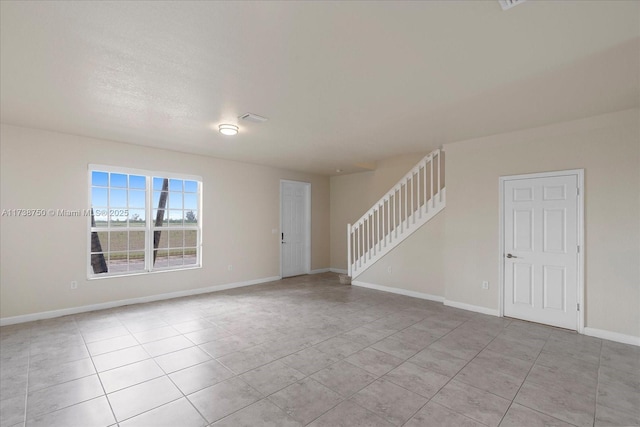 empty room featuring light tile patterned flooring, baseboards, and stairs