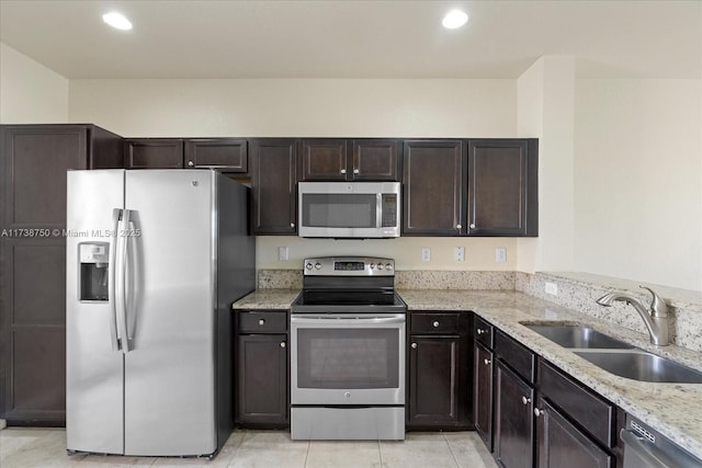 kitchen featuring dark brown cabinets, appliances with stainless steel finishes, light stone counters, and a sink