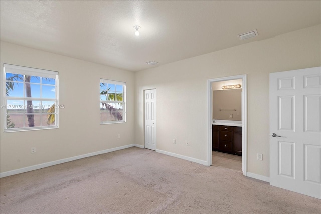 unfurnished bedroom featuring light carpet, ensuite bath, and baseboards