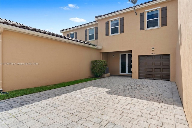 rear view of house with a garage, a tiled roof, decorative driveway, a patio area, and stucco siding