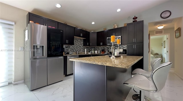 kitchen featuring appliances with stainless steel finishes, tasteful backsplash, a breakfast bar area, a center island, and light stone counters