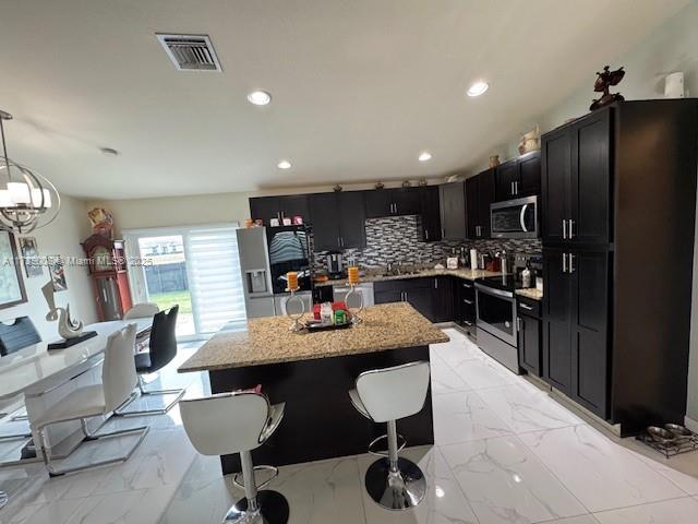 kitchen featuring hanging light fixtures, stainless steel appliances, light stone counters, a kitchen island, and decorative backsplash